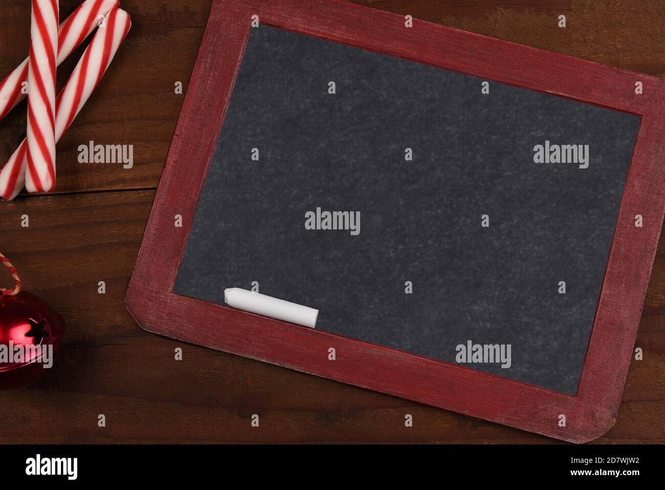 Una lavagna in ardesia bianca vintage con bastoncini di pepe e una campana di jingle rossa su una superficie di legno rustico. Foto Stock