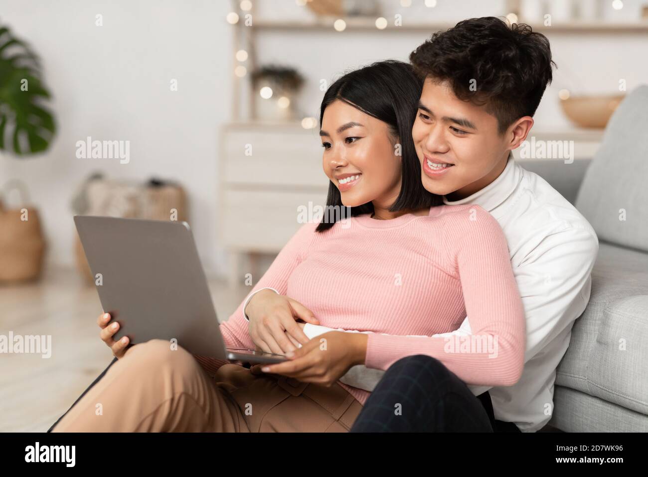 Felice coppia coreana che usa il laptop guardando film online a casa Foto Stock