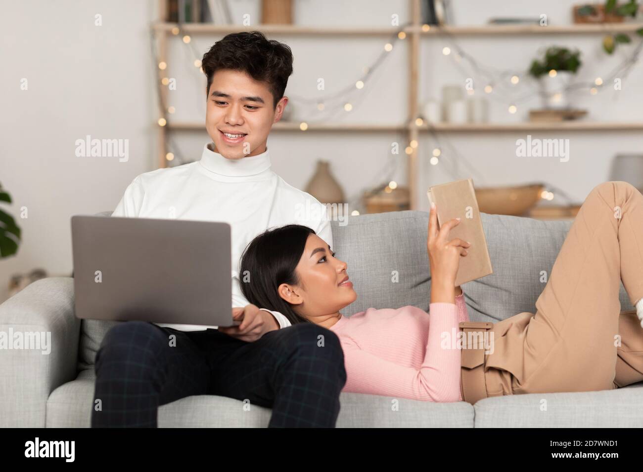 I coniugi giapponesi si rilassano con il laptop e il libro nel soggiorno Foto Stock