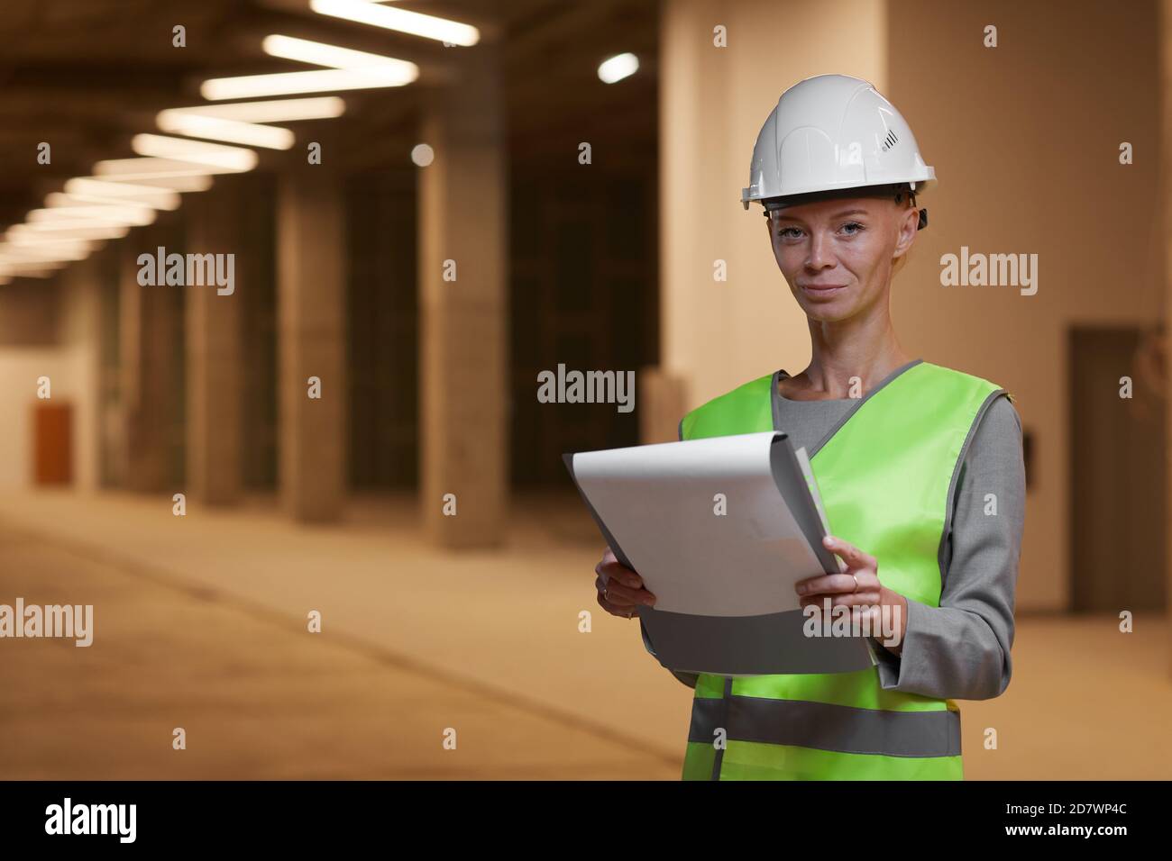 Vita in su ritratto della lavoratrice matura indossando il hardhat e guardando la macchina fotografica mentre si trova in cantiere all'interno, spazio di copia Foto Stock