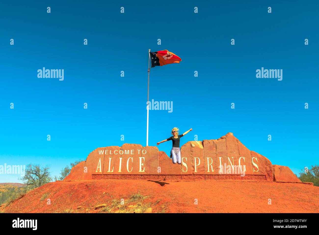 Carefree turista donna jumping a Alice Springs Welcome Sign in Northern Territory, Central Australia. Turismo nel deserto dell'Outback Red Centre. Viaggi Foto Stock