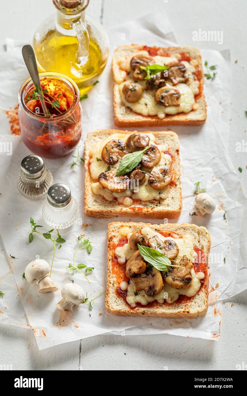 Toast croccante con funghi, basilico e formaggio su carta bianca Foto Stock