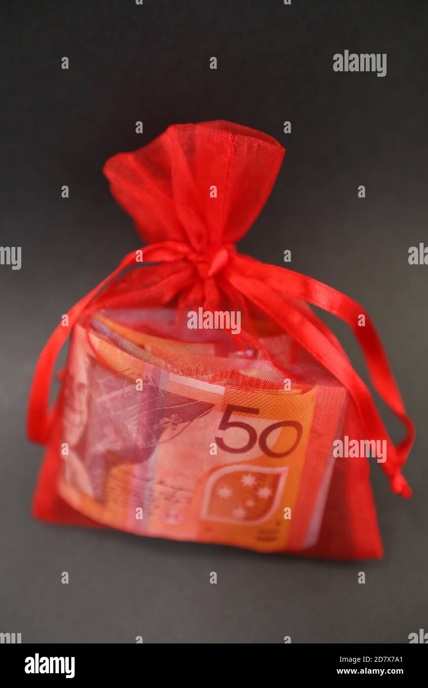 Una graziosa piccola borsa regalo rossa isolata con nastri di seta riempiti di denaro contante. 50 dollari nota visibile e wads di altre note colorate. Foto Stock