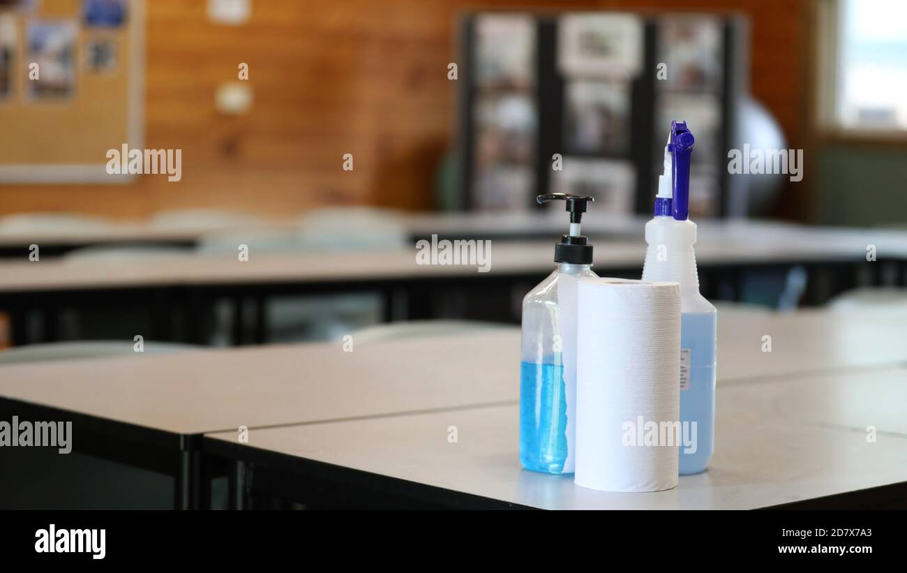 ambiente scolastico sicuro. Una stanza vuota con scrivanie e tavoli per studenti. Flacone con pompa igienizzante per mani blu e spray disinfettante. Foto Stock