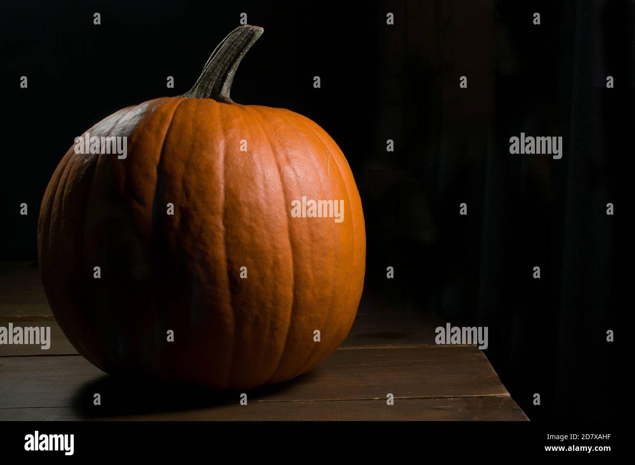 Zucca di Halloween su un tavolo rustico di legno con luce moody e una luce bordo con sfondo nero, concetto di celebrazione di Halloween Foto Stock