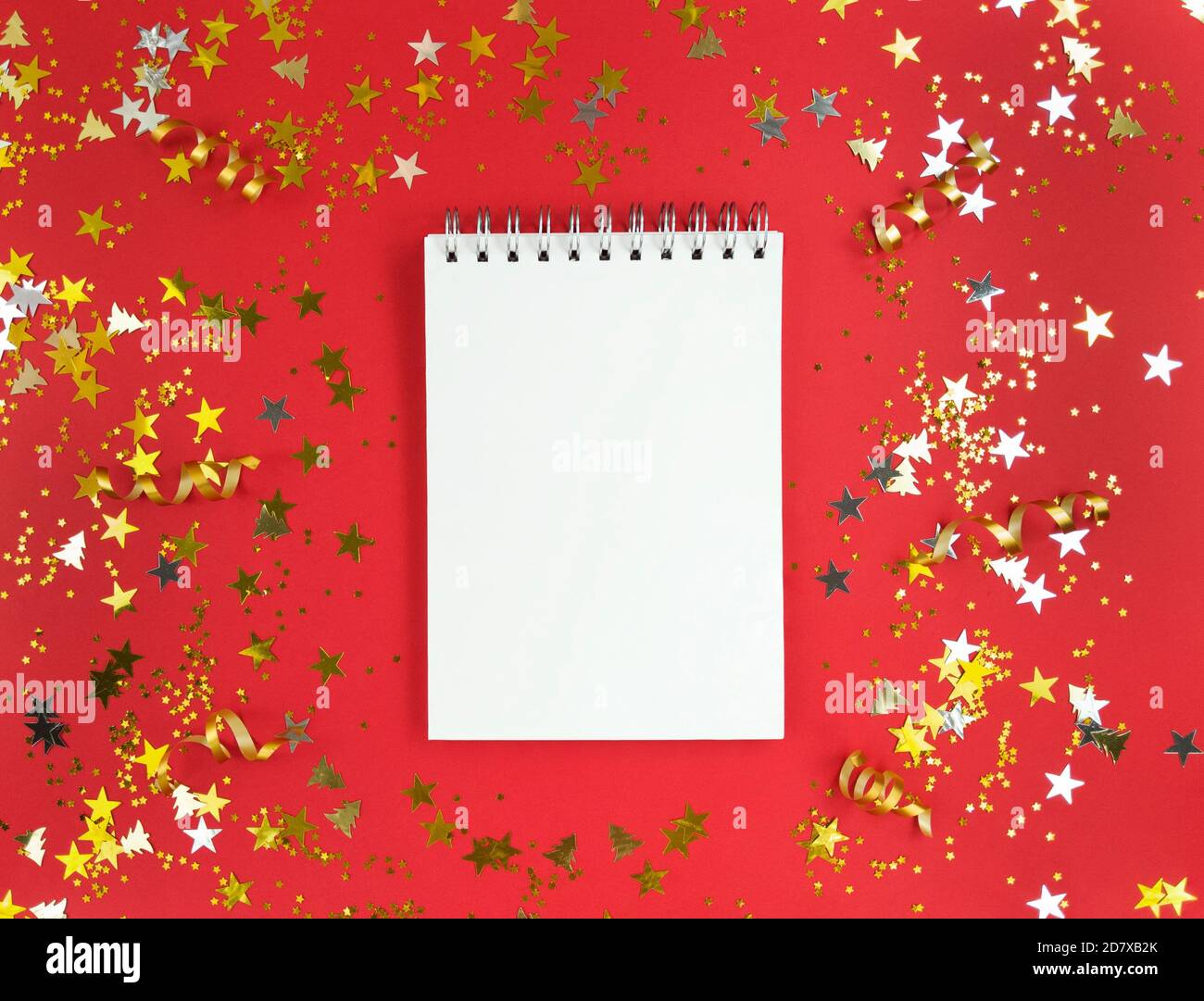 Foglio bianco di quaderno su sfondo rosso con confetti sparsi. Concetto di educazione alle vacanze. Foto di scorta. Foto Stock