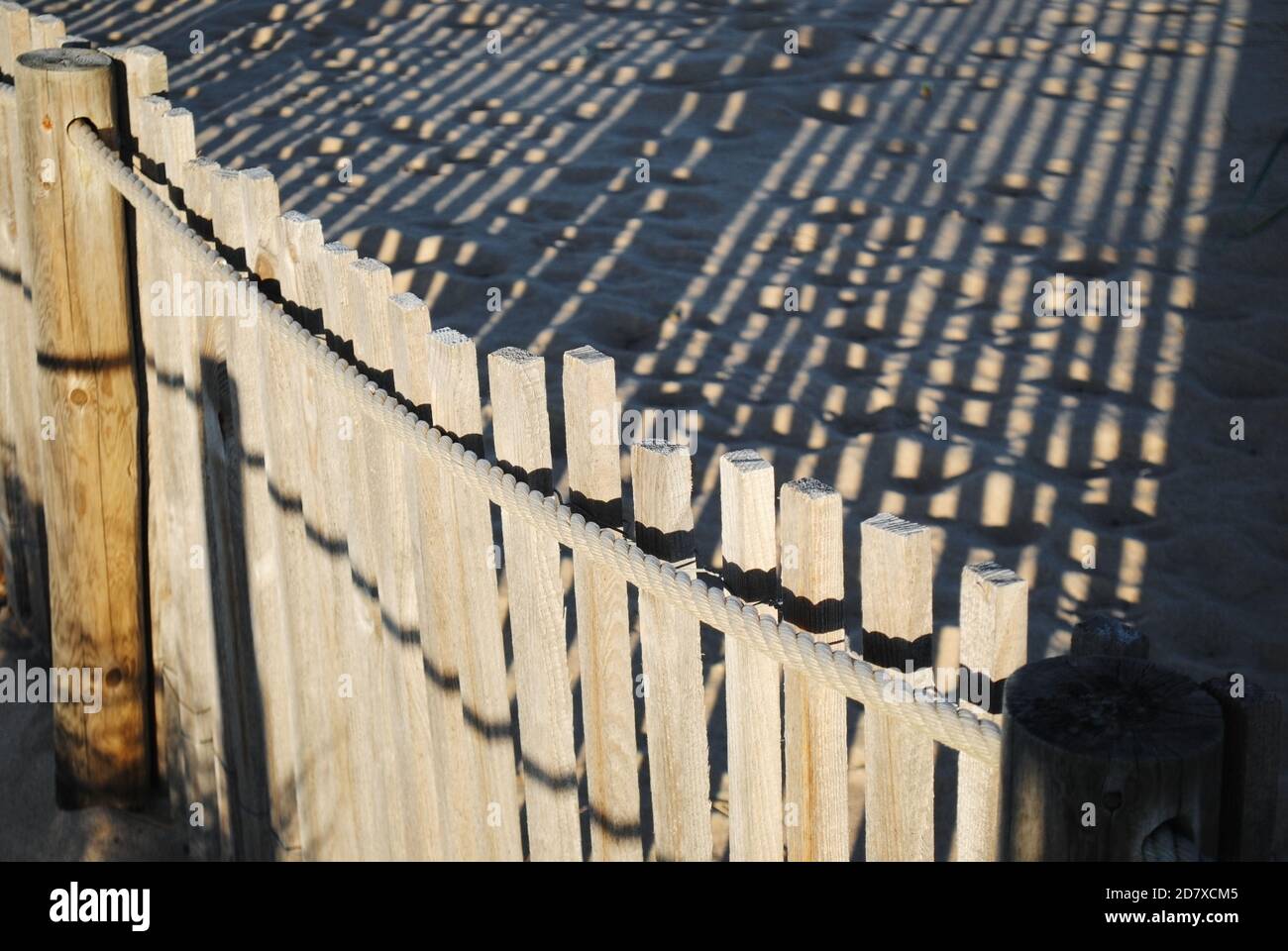 Una recinzione in legno con le sue ombre che si riflettono sulle dune di sabbia di Guincho, Portogallo. Foto Stock