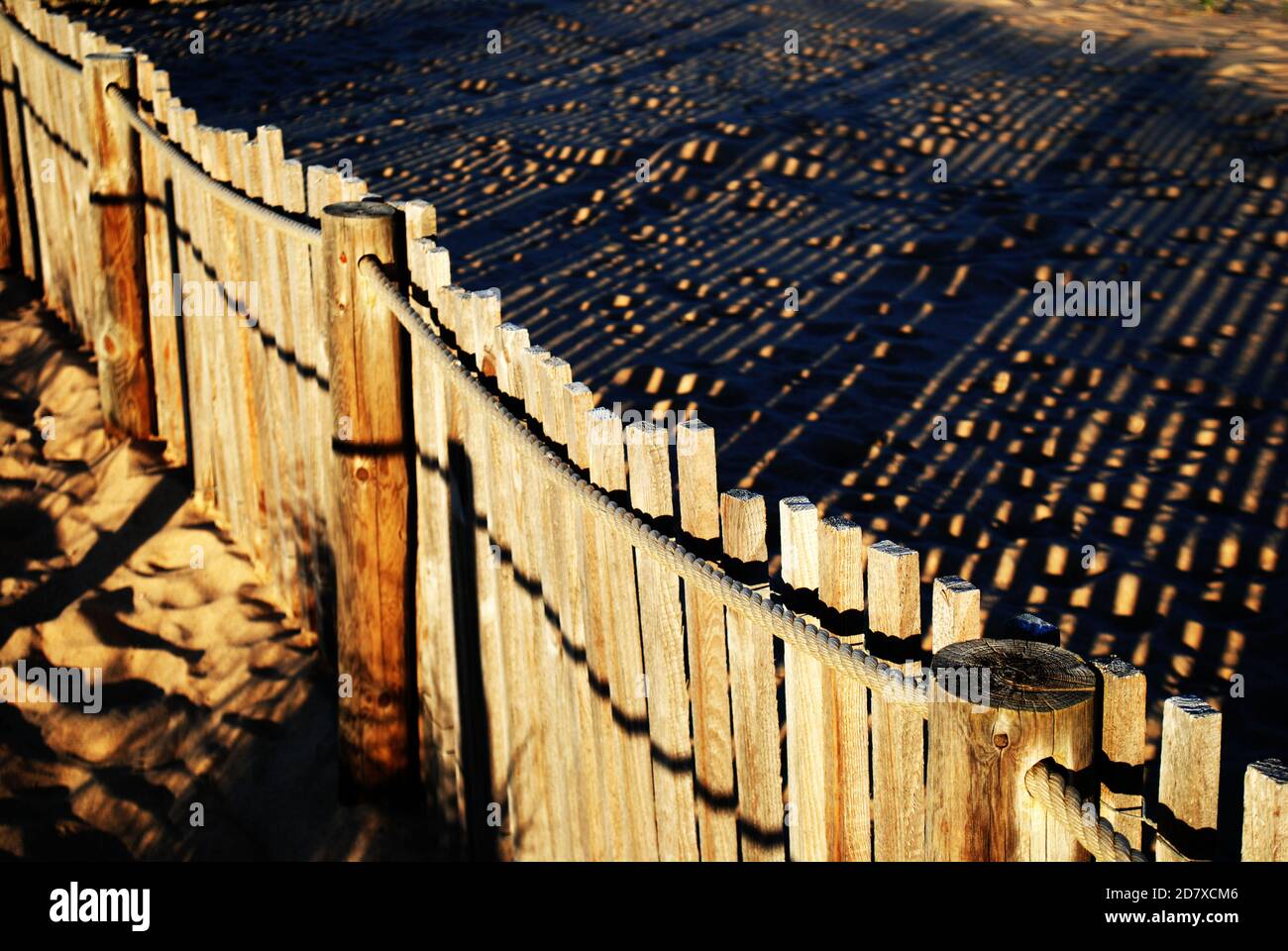 Una recinzione in legno con le sue ombre che si riflettono sulle dune di sabbia di Guincho, Portogallo. Foto Stock