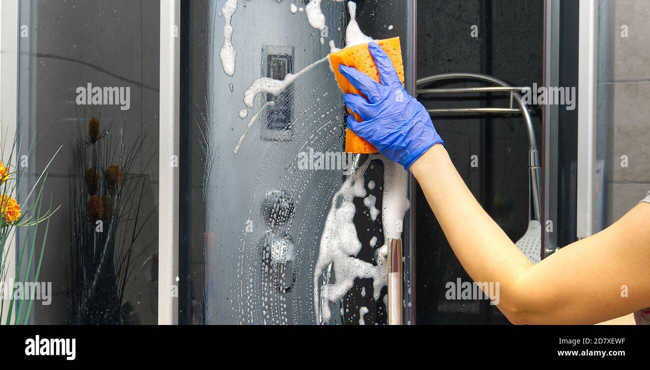 Pulizia delle cabine doccia vapore da depositi di calcio. Pulizia in bagno. Guanti da mano con straccio e detersivo doccia e vetro Foto Stock