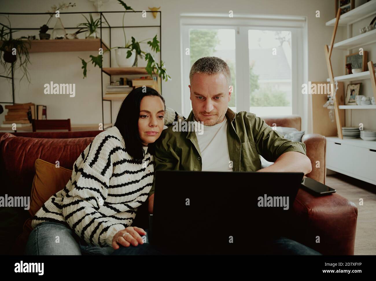 Marito e moglie seri usano il laptop mentre navigano a casa sedersi insieme sul divano Foto Stock