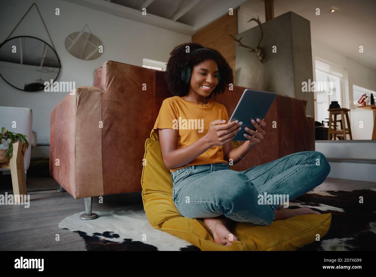 Vista ad angolo basso della giovane donna allegra che guarda il video mentre rilassarsi a casa utilizzando un tablet digitale con cuffie Foto Stock