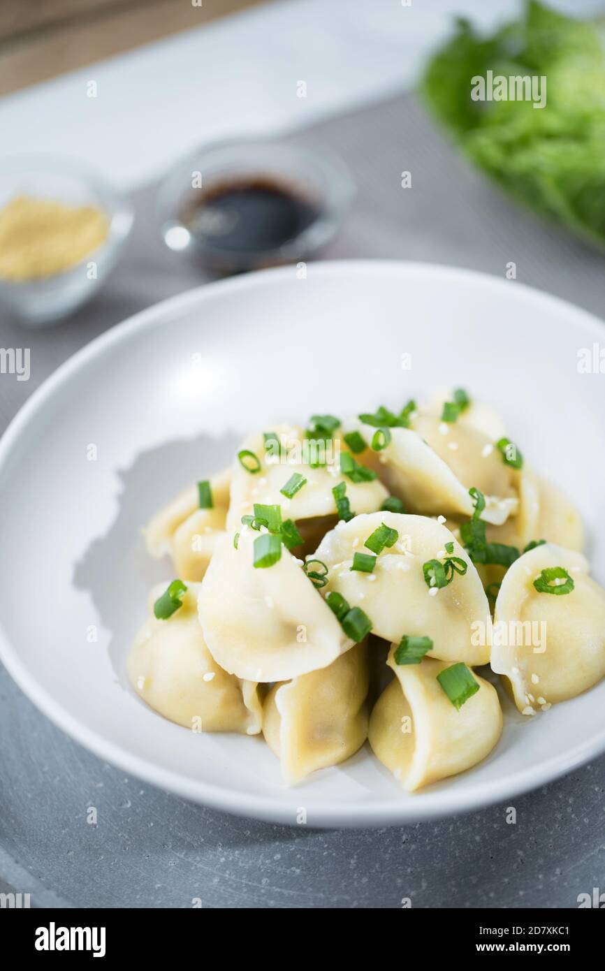 Gnocchi cinesi jiaozi nella piastra bianca sul grigio backrgound con cavolo cinese napa e semi di pesamo e soia salsa con un tovagliolo Foto Stock