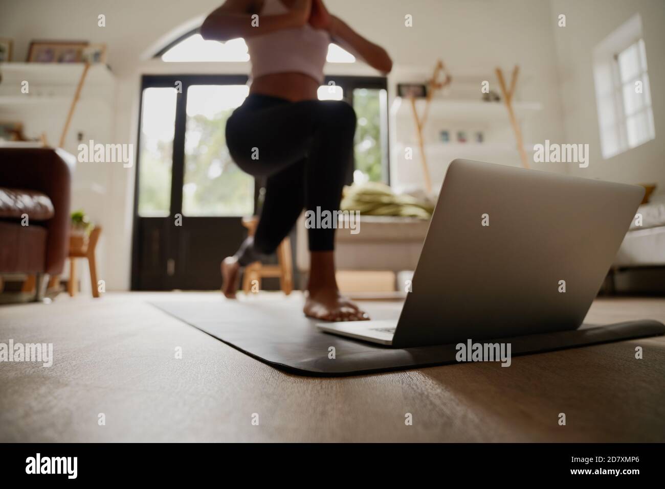 Primo piano del laptop sul tappetino fitness con la giovane donna che pratica esercizio di yoga con l'aiuto di video online Foto Stock