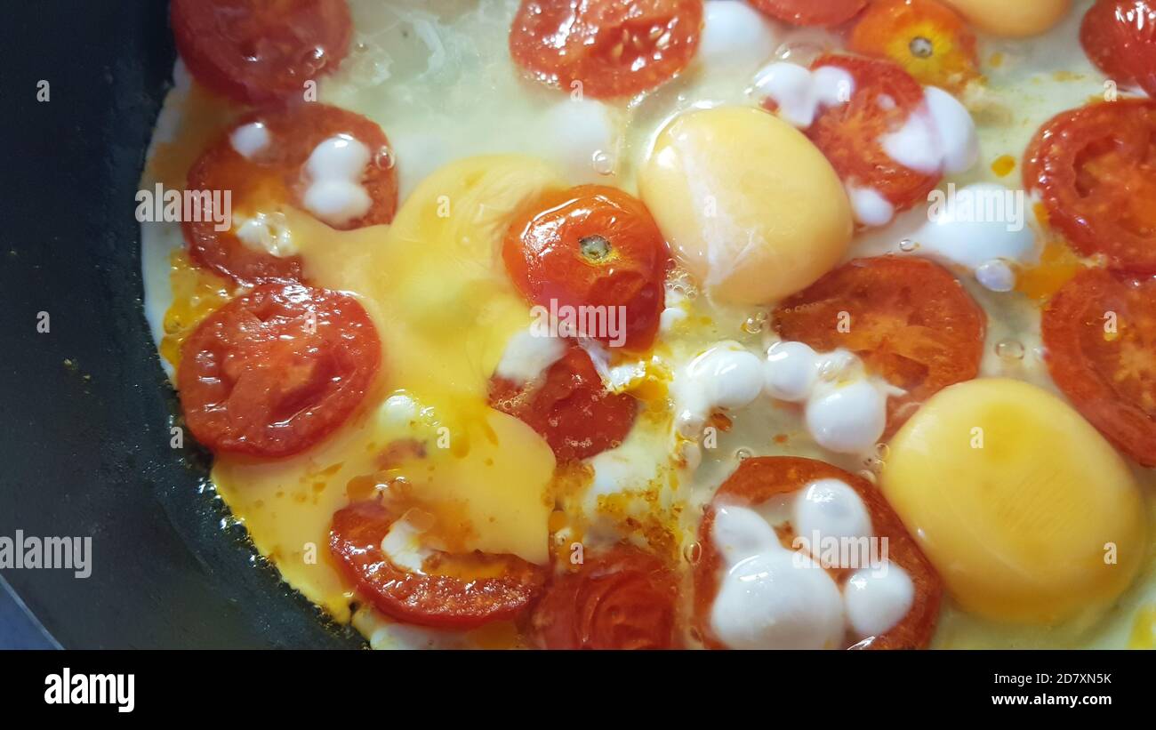 le uova strapazzate con fette rotonde di pomodori vengono cotte in una padella, primo piano Foto Stock
