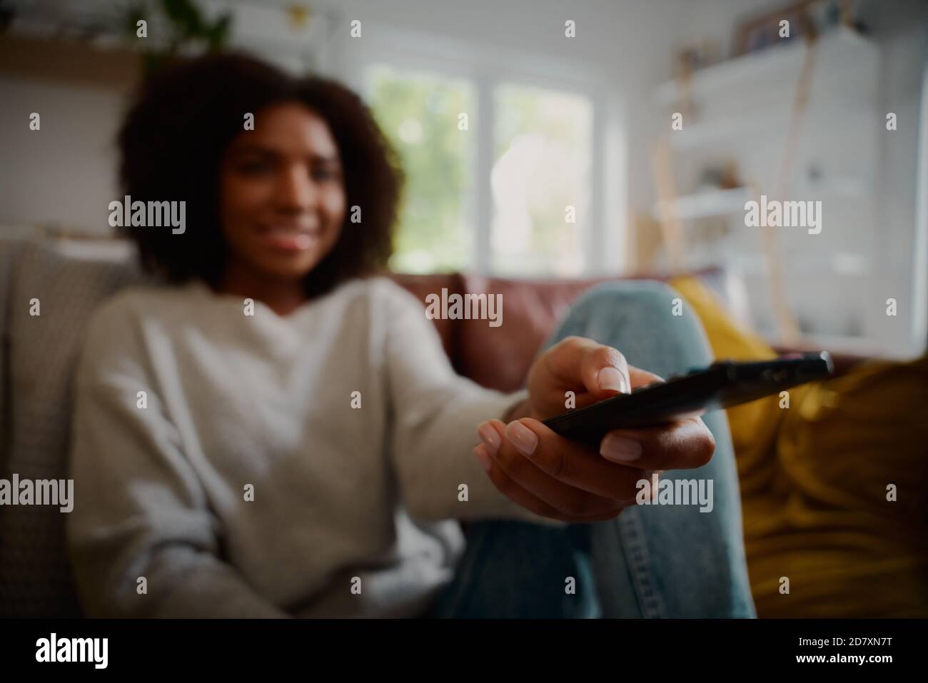 Primo piano di una donna che tiene il telecomando mentre si è seduti a. home guardare la televisione da solo Foto Stock