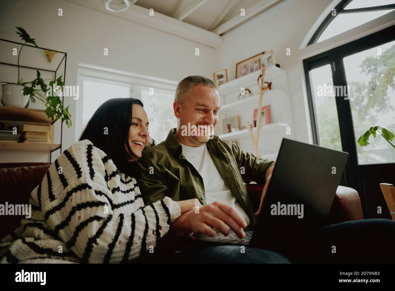 Bella giovane coppia amorosa guardando il computer portatile e sorridendo mentre seduti insieme sul divano Foto Stock