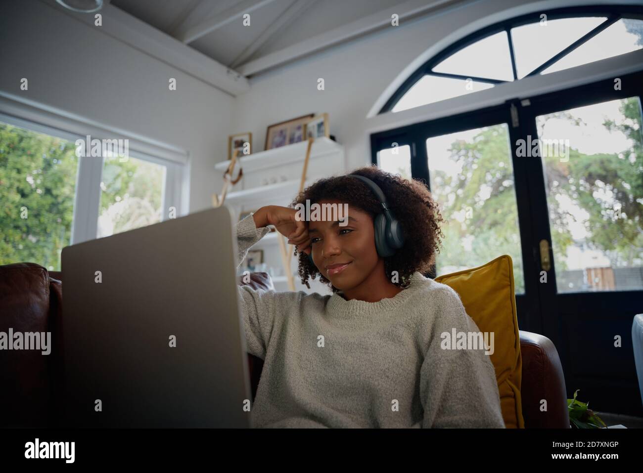Giovane donna nera che guarda il video sul computer portatile con le cuffie a. a casa mentre ci si rilassa sul divano Foto Stock
