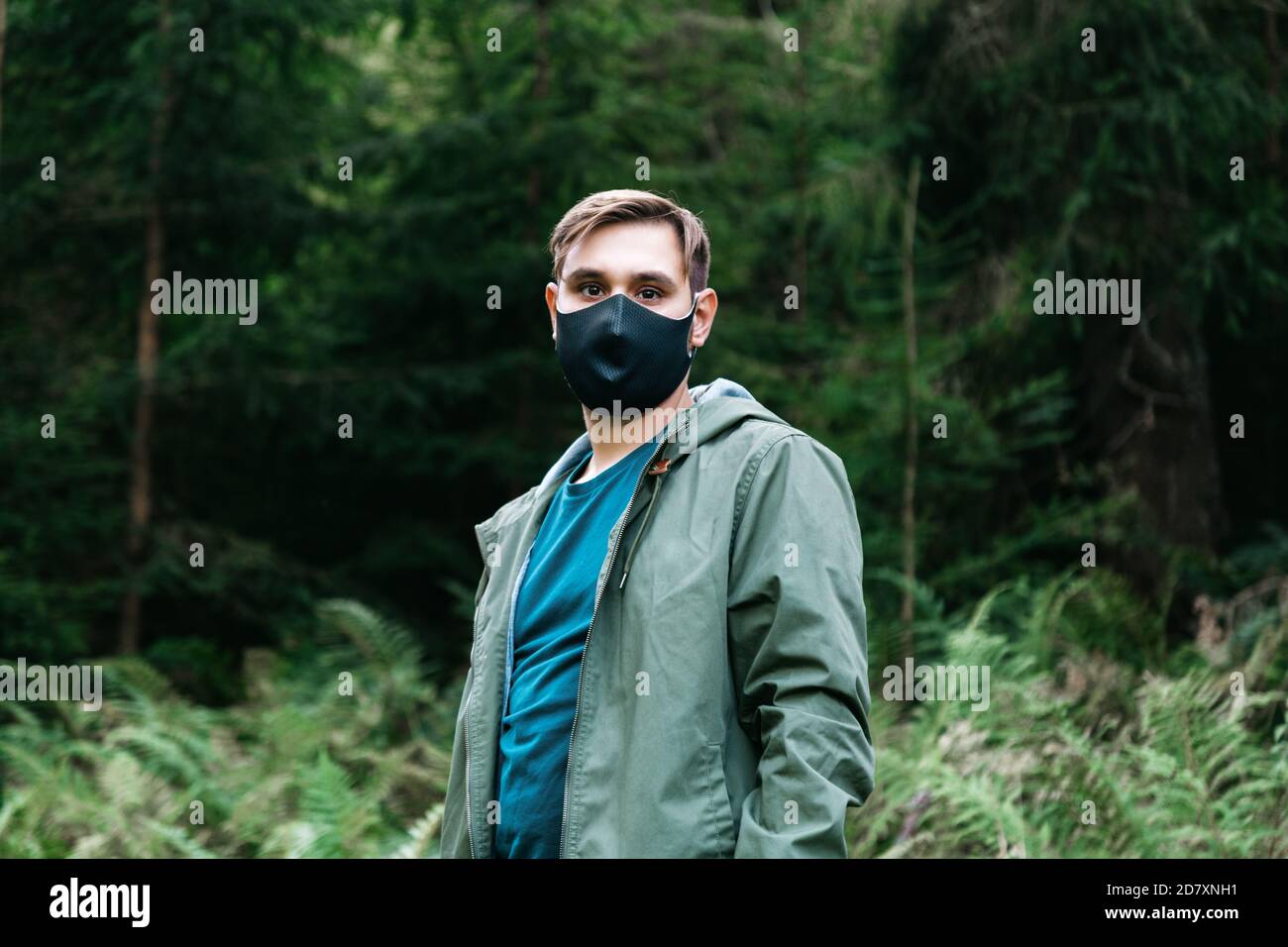Uomo in maschera medica protettiva nera fuori in foresta da solo. L'uomo viaggia da solo mantenendo la distanza sociale nel turismo locale. Protezione contro Foto Stock
