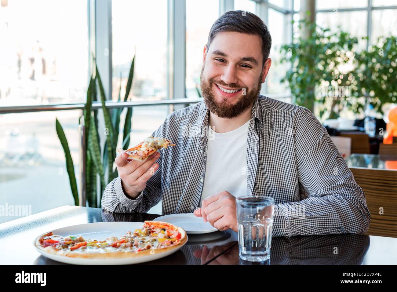 Ritratto felice sorridente uomo caucasico mangiare pizza italiana in pizzeria mantiene la distanza sociale. Deliziosa pizza al caffè. Foto Stock