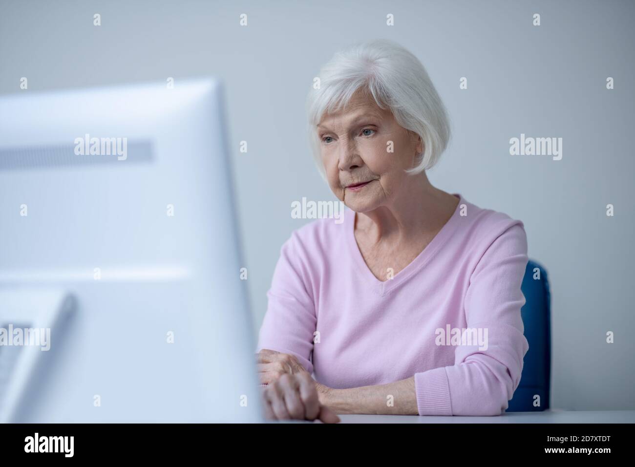 Donna anziana dai capelli grigi seduta davanti al computer Foto Stock