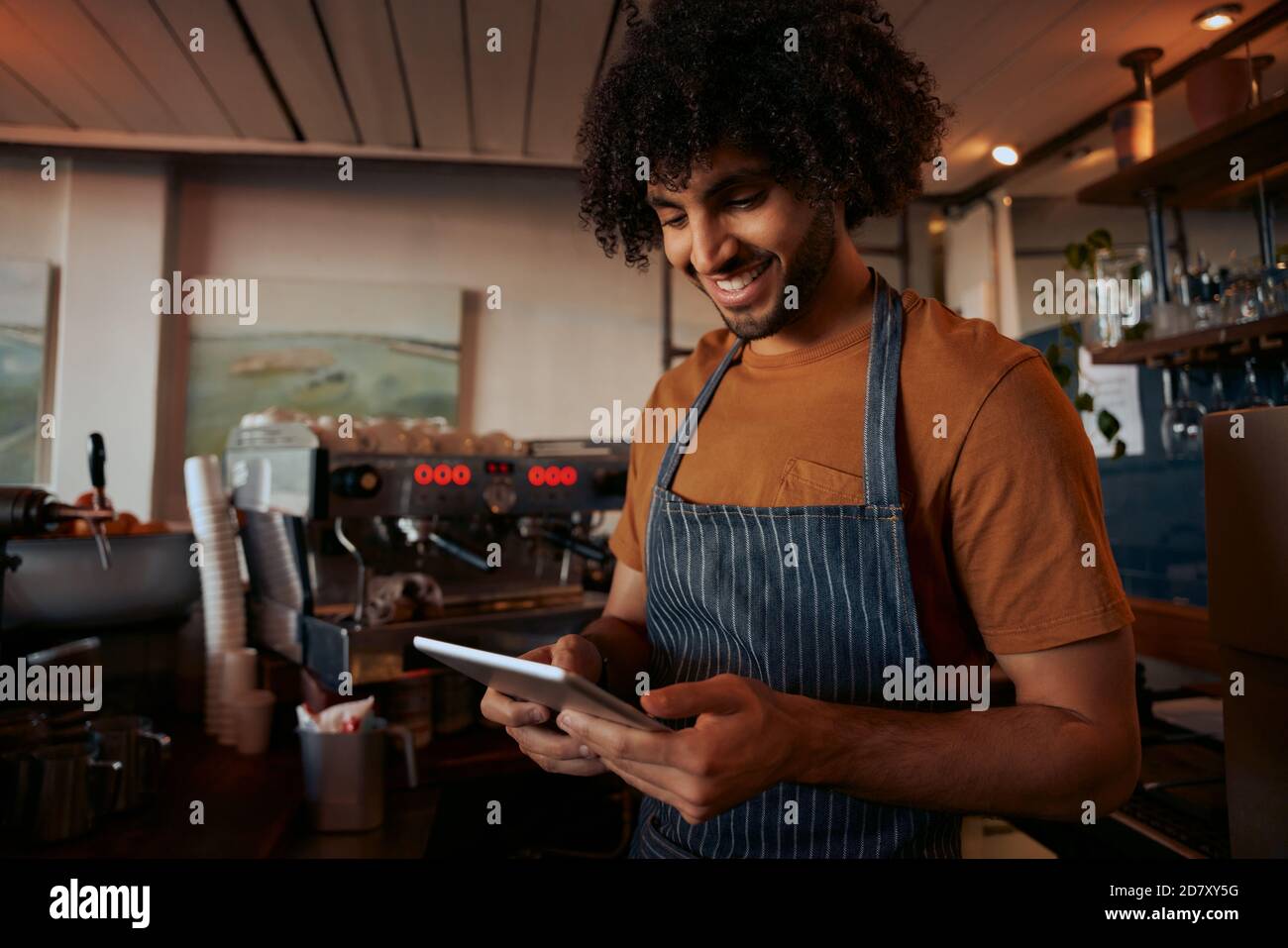 Giovane uomo in grembiule utilizzando digitale compressa al suo cafe Foto Stock