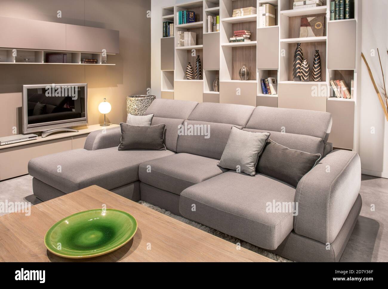 Grande e confortevole divano beige in un intimo soggiorno interno con televisore e display a parete, vista su un caffè tavolo con terracotta verde pla Foto Stock