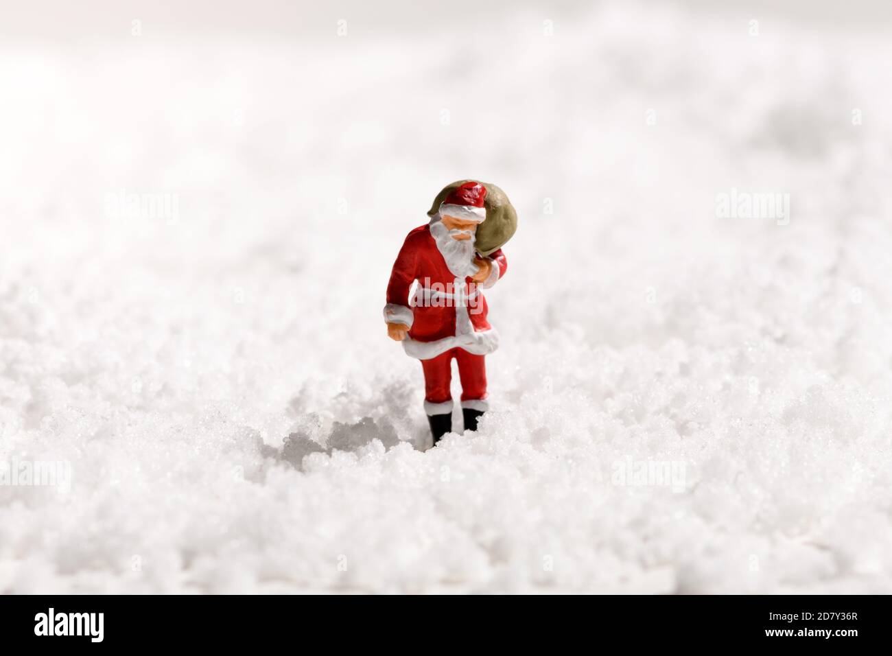 Babbo Natale in miniatura con un sacco pieno di regali a piedi attraverso neve fresca bianca invernale con spazio per la copia per il Saluto di Natale stagionale Foto Stock