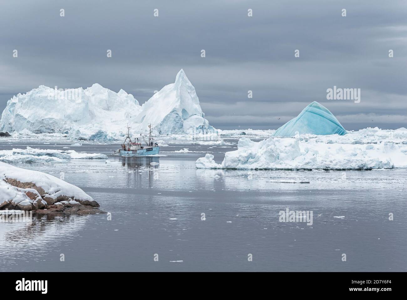 Una barca Fisher sta navigando tra gli iceberg. La barca blu circondata da iceberg. Ilulissat, Patrimonio dell'Umanità dell'UNESCO, Baia di Disko, Groenlandia. - Foto Stock