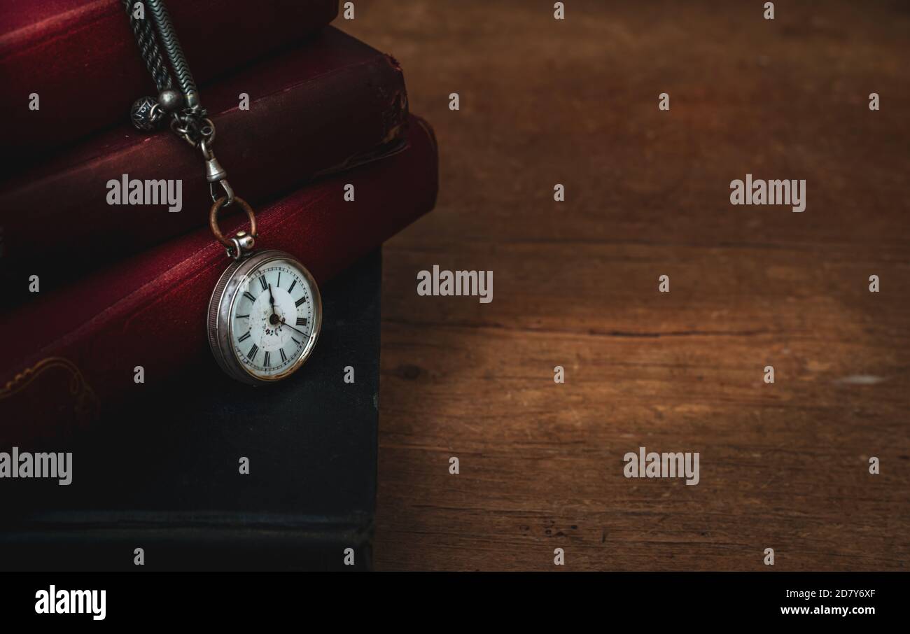 vecchi libri accatastati sul tavolo con orologio tascabile, moody con spazio per il testo, concetto di passsing del tempo. Foto Stock