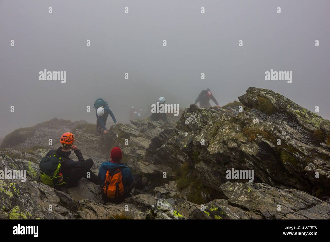 Gruppo di alpinisti che indossano caschi riposano nella nebbia sulle rocce sulla cima della montagna dopo aver sguazzato nel Lake District in Inghilterra. Foto Stock