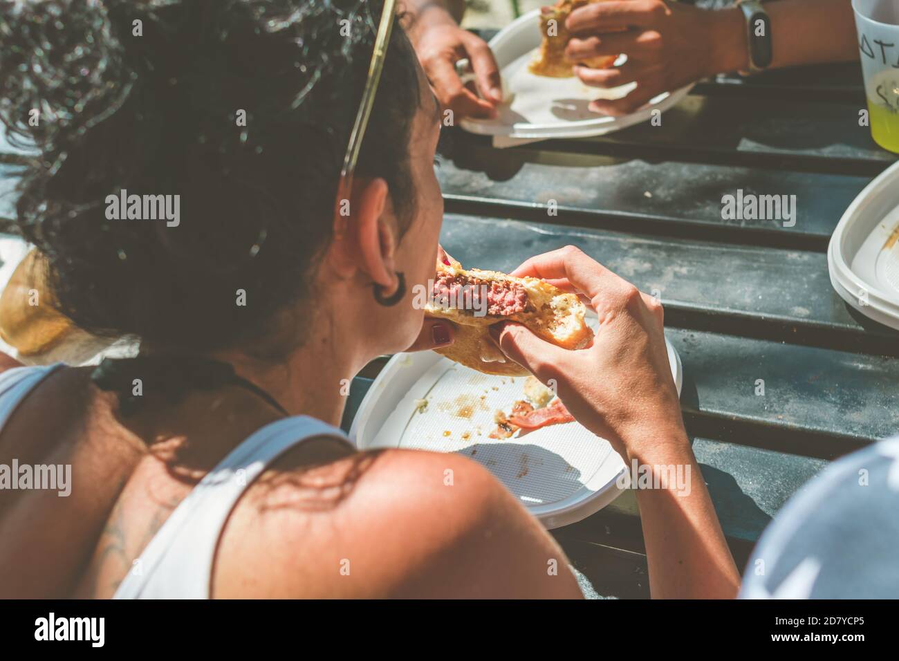 giovane donna da dietro mangiare hamburger sul campo Foto Stock