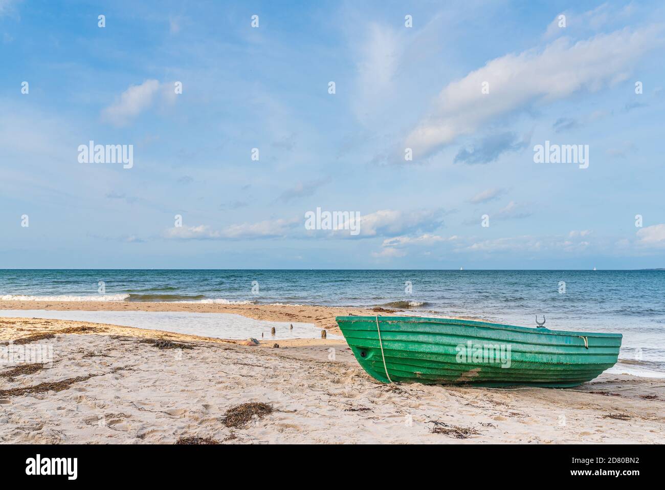 piccola barca verde su spiaggia di sabbia vuota contro il mare e. cielo blu Foto Stock