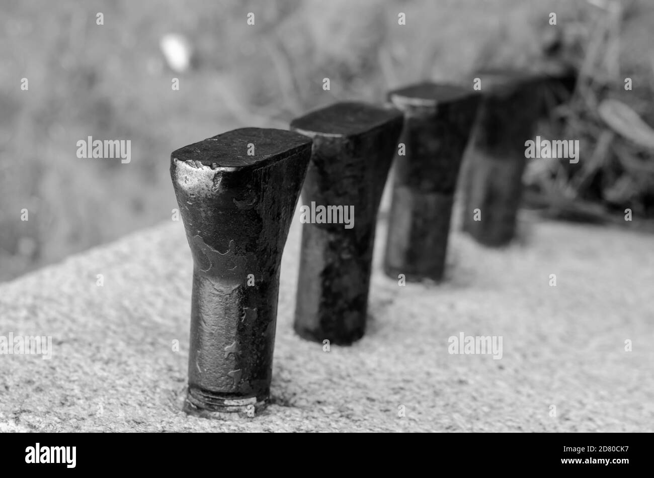 Fila di ancoraggi in metallo avvolti in primo piano in pietra. Vecchie ancore arrugginite in cemento. Astrazione architettonica. Senza persone. Foto Stock