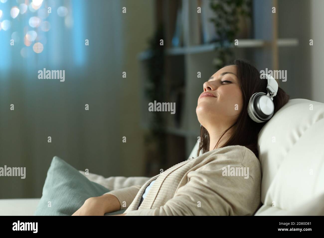 Donna rilassata seduta su un divano che ascolta la musica la notte a casa Foto Stock