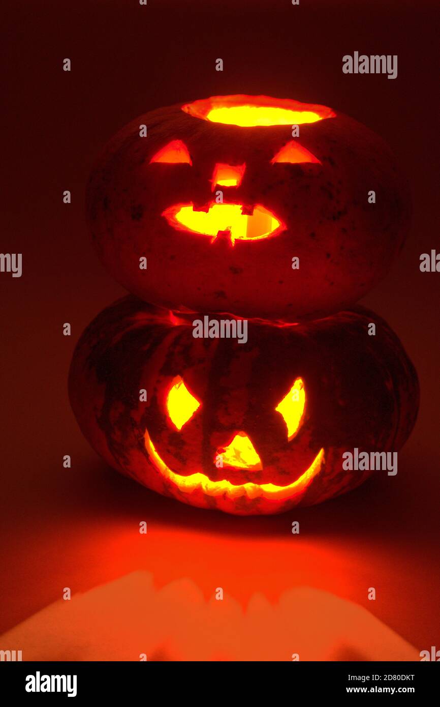 zucca di halloween su altra zucca di halloween. misteriosa luce rossa e riflessi. scolpiti volti spaventosi Foto Stock