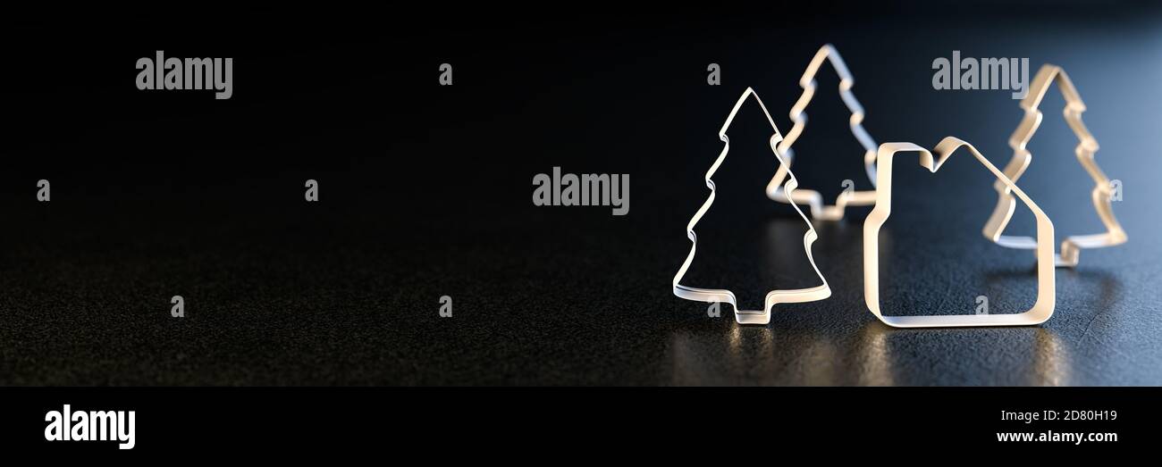 Concetto di bene immobile di Natale: Una taglierina a forma di casa del biscotto e tre taglienti del biscotto dell'albero di Natale che si levano in piedi su una piastra metallica nera. Dimensione banner Web. Foto Stock