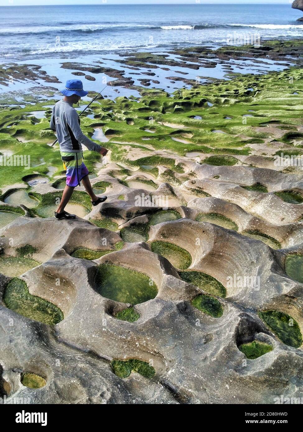 Pescatore balinese locale che cammina lungo rocce erose e muschio verde a Balangan Beach, Bali, Indonesia Foto Stock