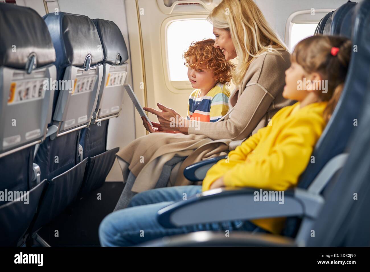 Donna all'interno di un aereo che mostra una tavoletta ad un ragazzo Foto Stock