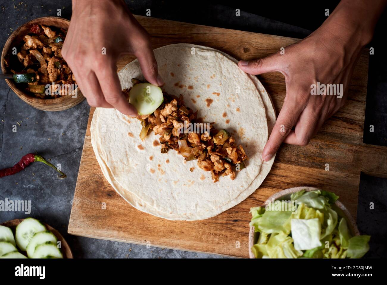 vista ad alto angolo di un giovane caucasico che prepara un durum o un burrito, con carne di pollo cotta con verdure diverse come cipolla o rosso e g Foto Stock