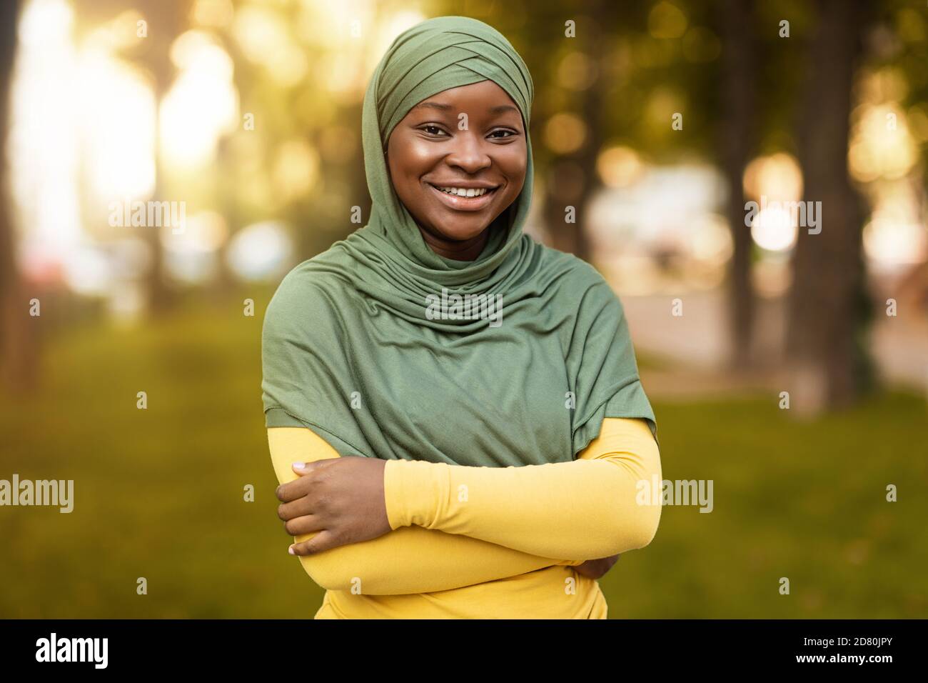 Donna musulmana nera sorridente in piedi Hijab con armi piegate All'aperto Foto Stock