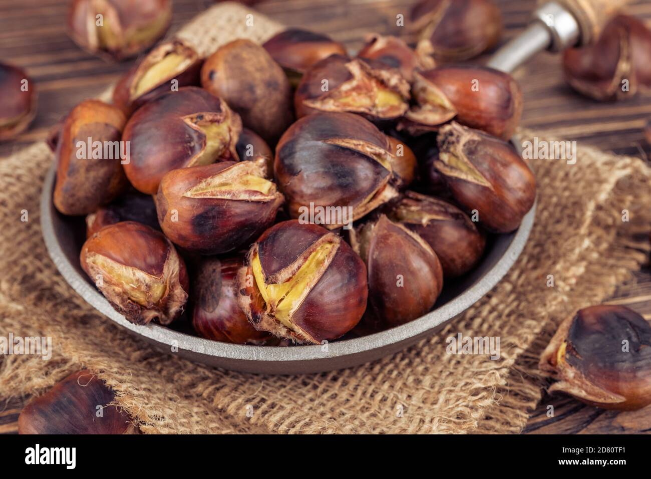 Castagne in una padella su sfondo ligneo. Stile rustico Foto Stock