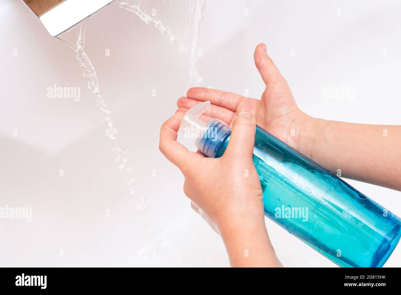 Un bambino versa sapone o antisettico sulle mani sotto un rubinetto con acqua pulita da vicino su uno sfondo bianco. Concetto di igiene. Prevenzione delle malattie, salute Foto Stock