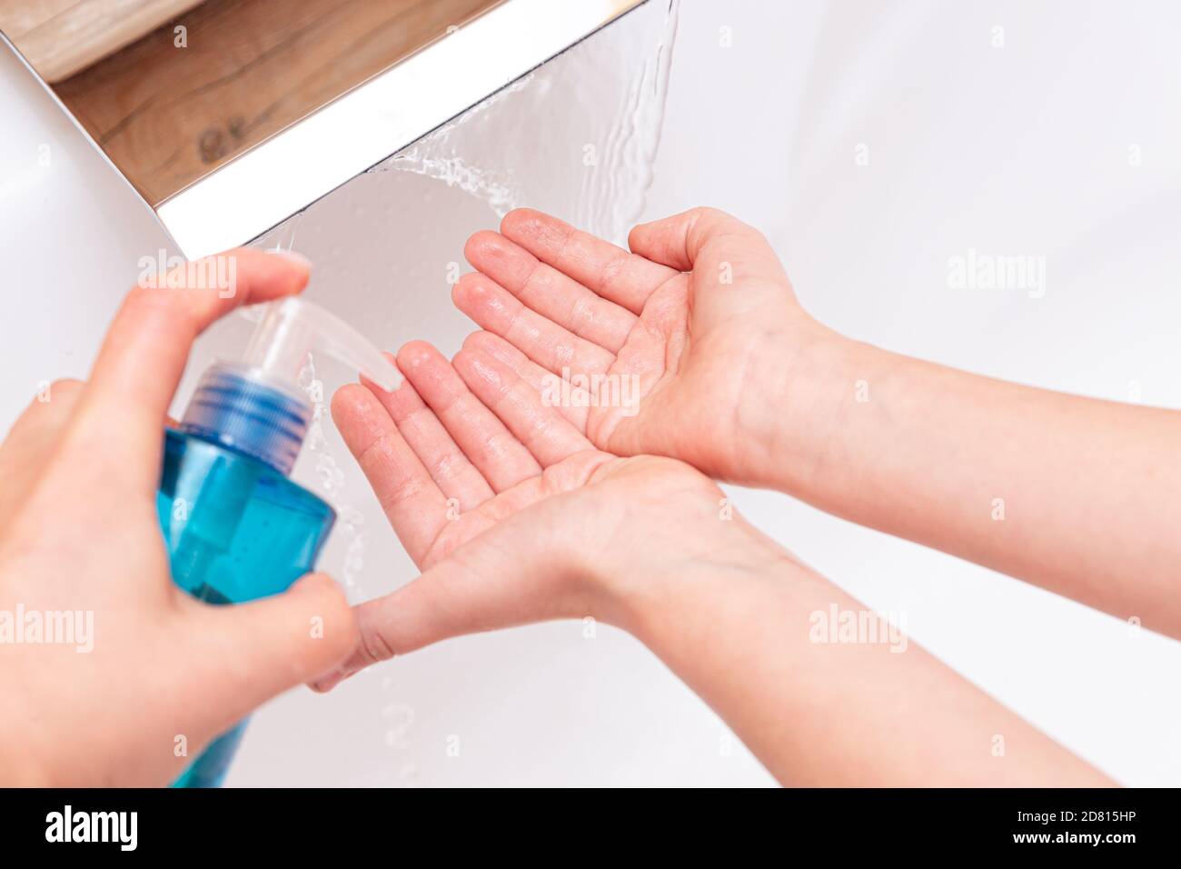 Le mani versano sapone o antisettico sulle mani del bambino sotto un rubinetto con acqua pulita da vicino su uno sfondo bianco. Concetto di igiene. Malattia preven Foto Stock