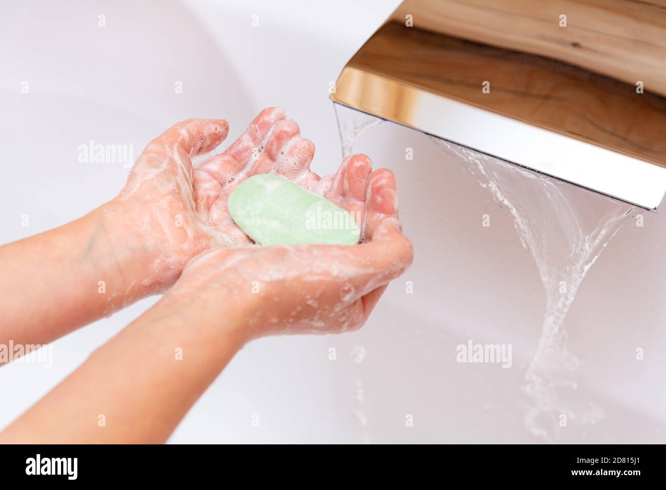Il bambino le lava le mani con sapone sotto l'acqua corrente. Un pezzo di sapone verde nelle mani dei bambini da vicino. Concetto di igiene. Malattia preven Foto Stock
