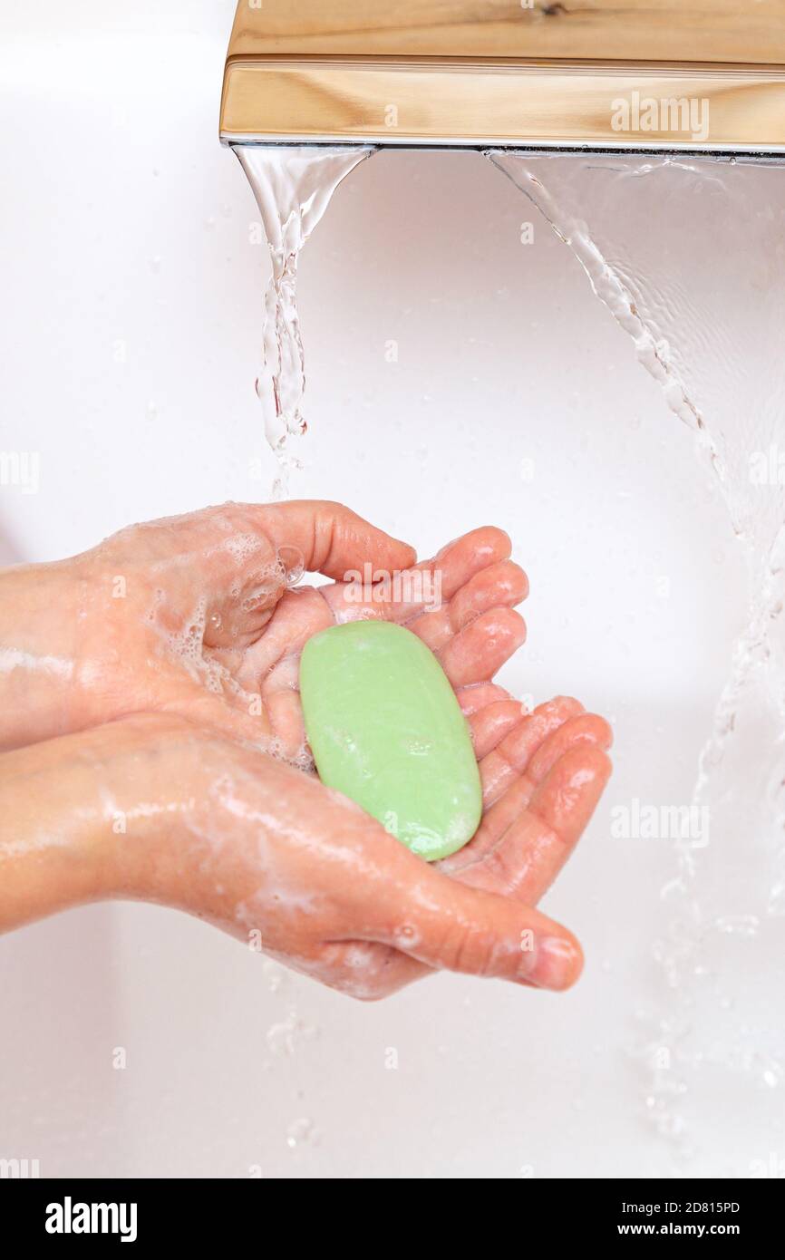 Il bambino le lava le mani con sapone sotto l'acqua corrente. Un pezzo di sapone verde nelle mani dei bambini da vicino. Concetto di igiene. Malattia preven Foto Stock