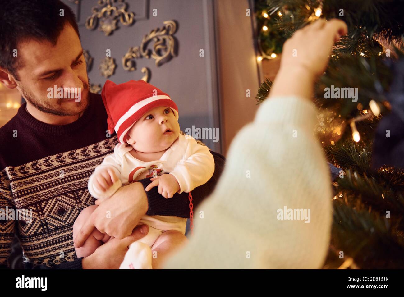 Padre e madre con il loro bambino che decorano l'albero insieme dentro camera Foto Stock