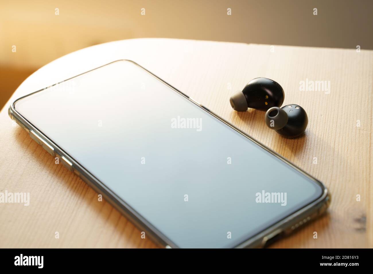 Auricolari wireless e uno smartphone su un tavolo di legno Foto Stock