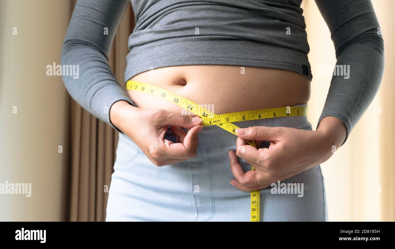 Grasso donna mano tenuta nastro di misurazione sul suo ventre grasso. Donna dieta stile di vita e costruire il concetto muscolare. Foto Stock