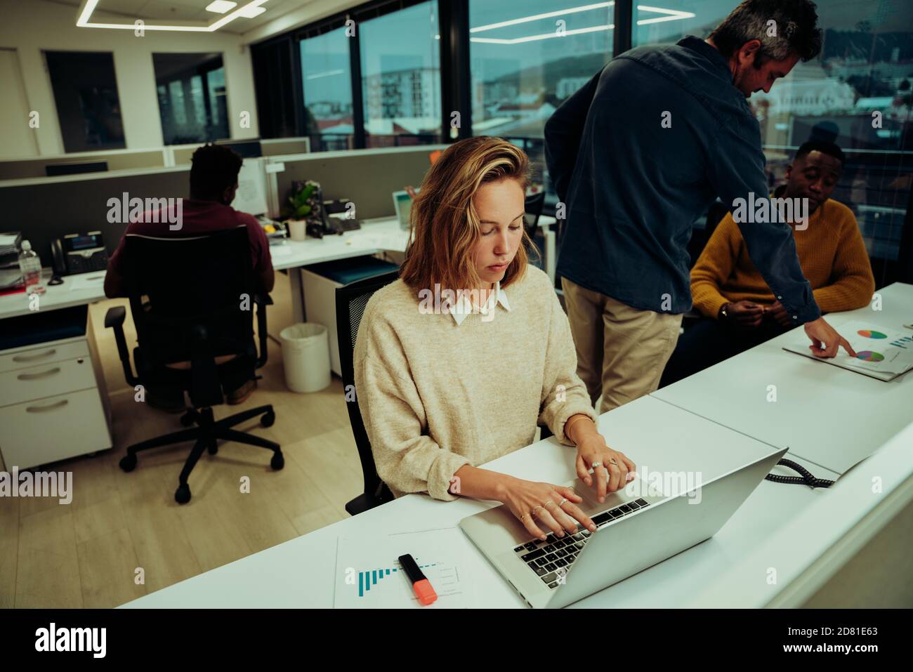 Giovane donna di affari che scrive il email sul laptop al capo e i clienti che cercano serii Foto Stock