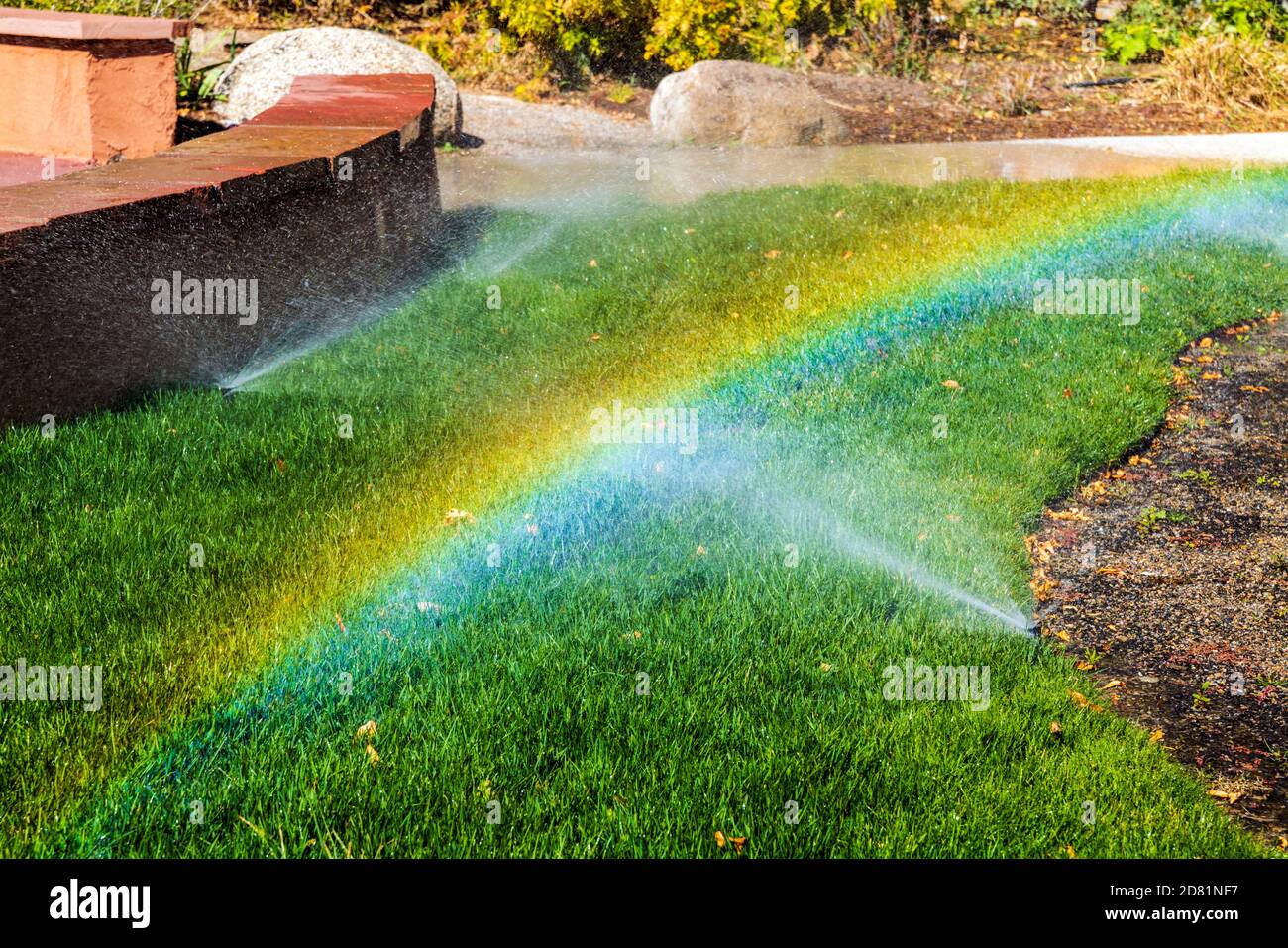 Gli irrigatori e il sole creano un arcobaleno di colore Foto Stock